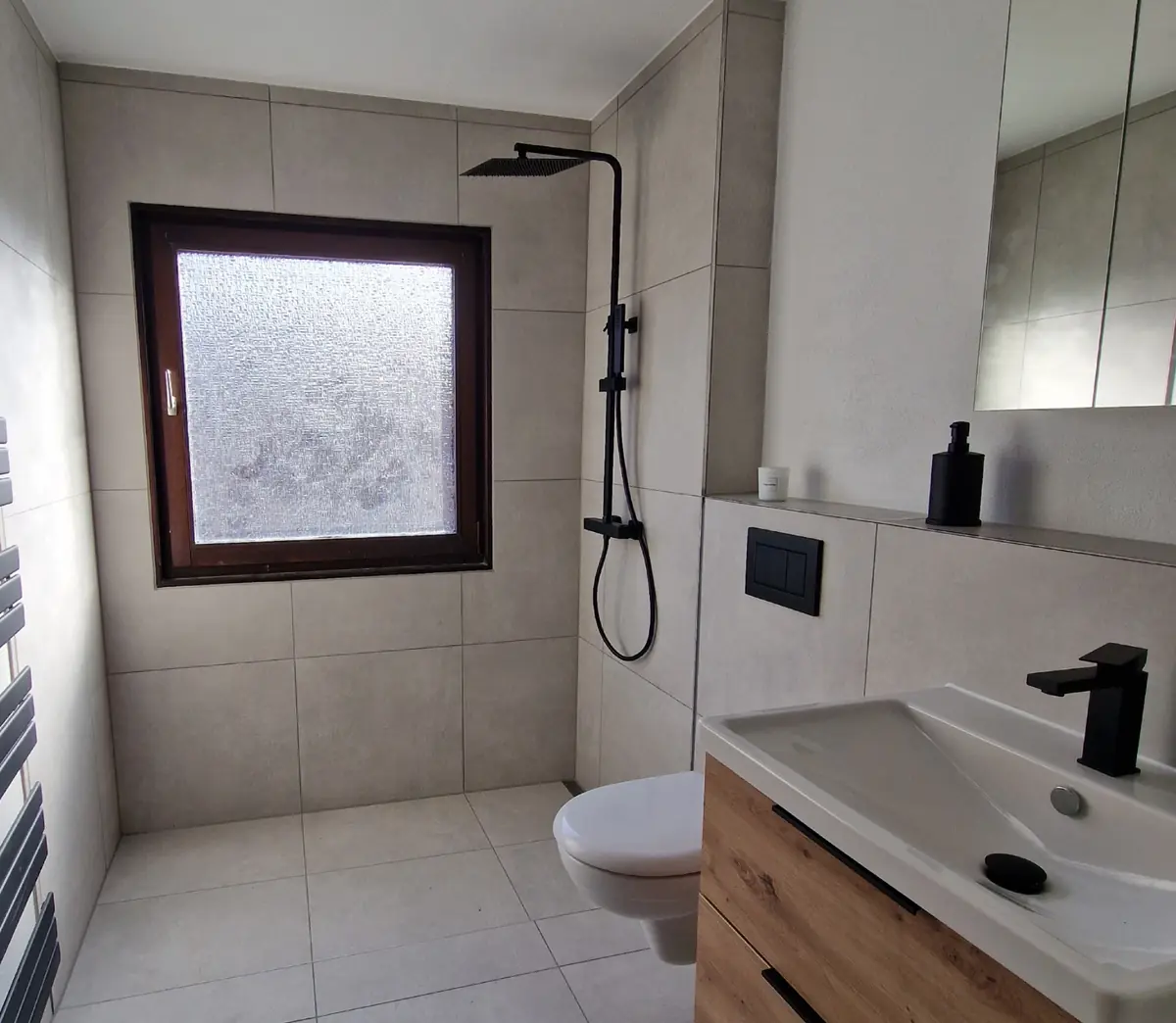 Helles Bad mit großformatigen Fliesen, bodengleicher Dusche und schwarzen Armaturen