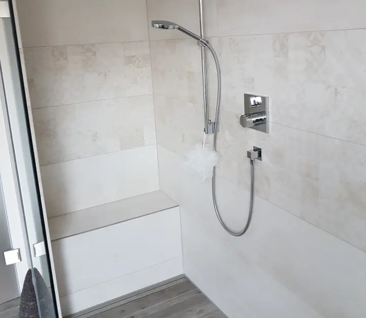Dusche mit Sitzbank und hellen Fliesen