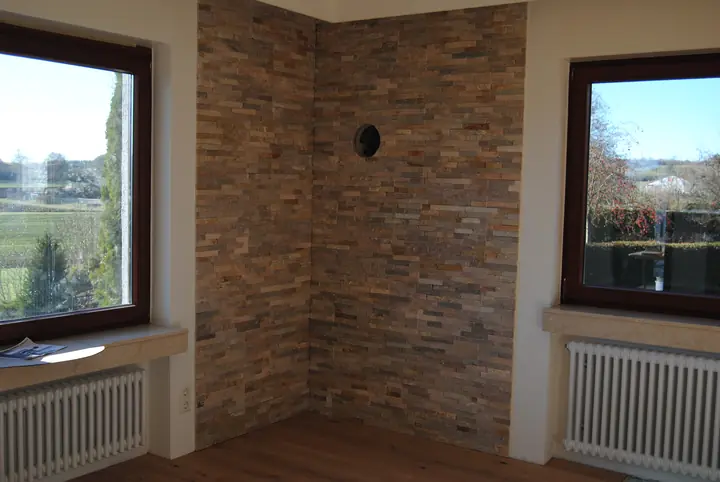 Wand mit Natursteinverblendern zwischen zwei Fenstern